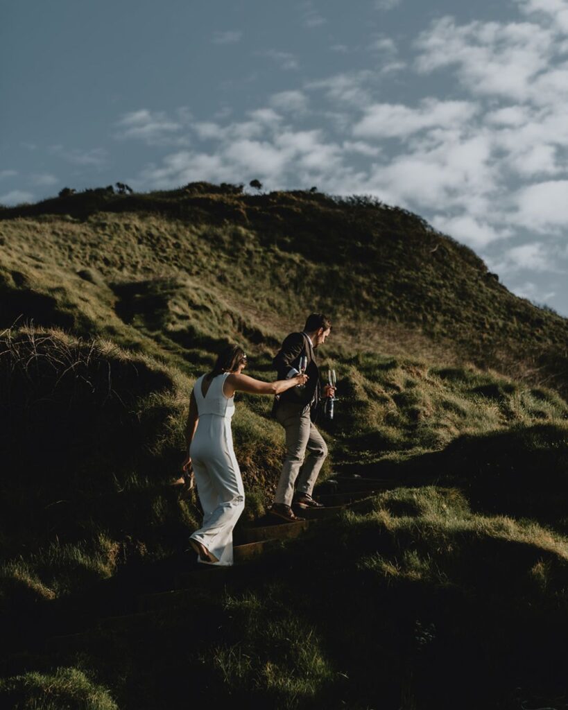 A couple eloping in Wales holding hands on a cliff at sunset overlooking the sea