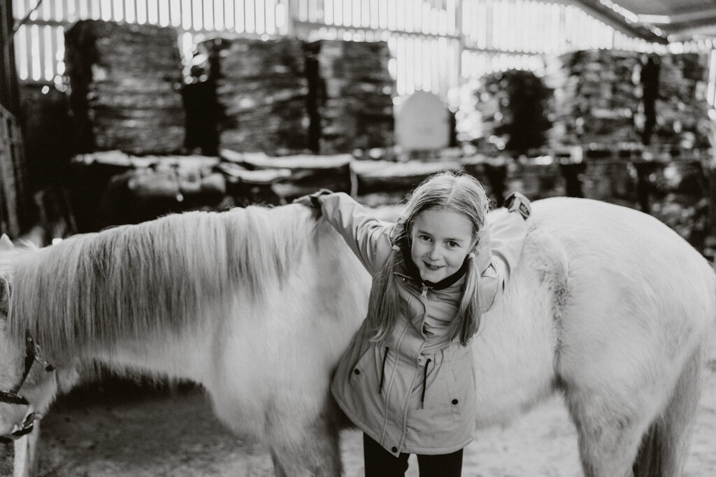 A natural family photoshoot in St Davids, Pembrokeshire, with a mother and daughter riding horses at sunset on the coast