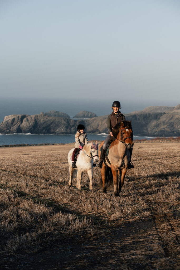 A natural family photoshoot in St Davids, Pembrokeshire, with a mother and daughter riding horses at sunset on the coast