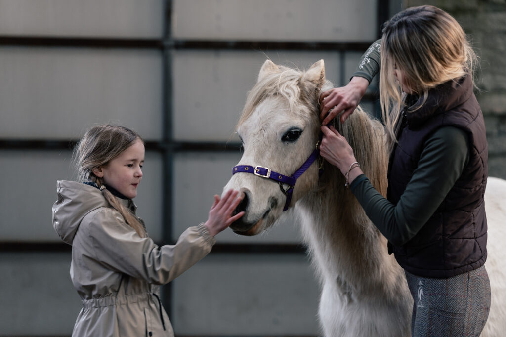 A natural family photoshoot in St Davids, Pembrokeshire, with a mother and daughter riding horses at sunset on the coast